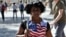 Una mujer camina vestida con una camiseta con la bandera de estadounidense por una calle de La Habana. 